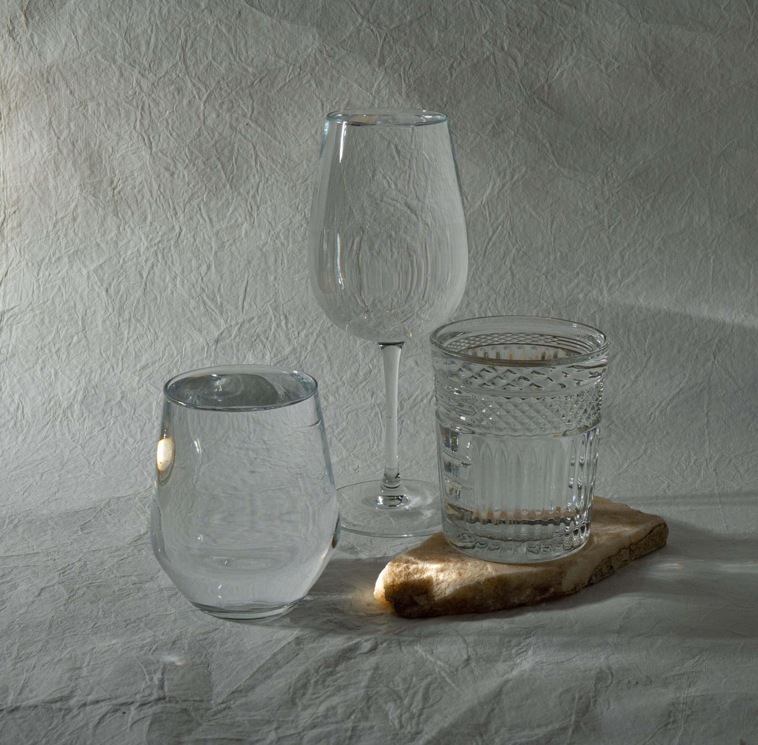 Home Elegant arrangement of glassware on a textured surface, showcasing light play and transparency.